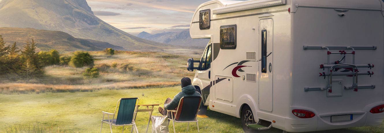 Man sits outside next to his RV looking at the mountains in the distance.