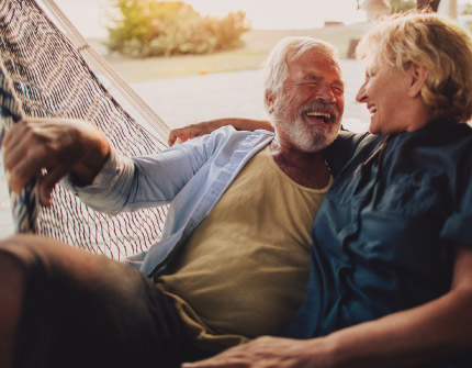 A mature man and woman enjoy each other's company while sitting in a hammock.