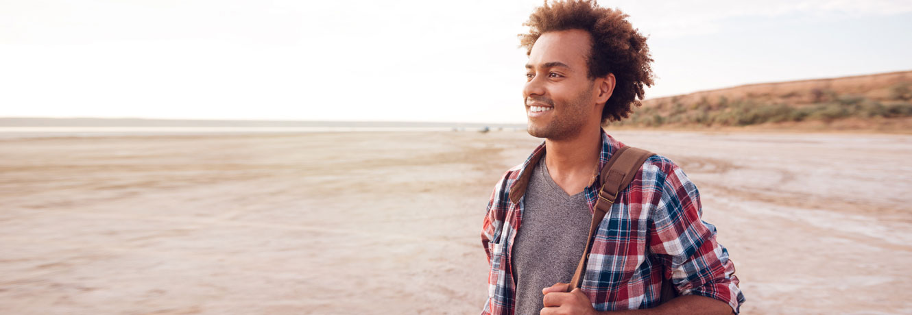 Young man on a beach looks off into the horizon smiling