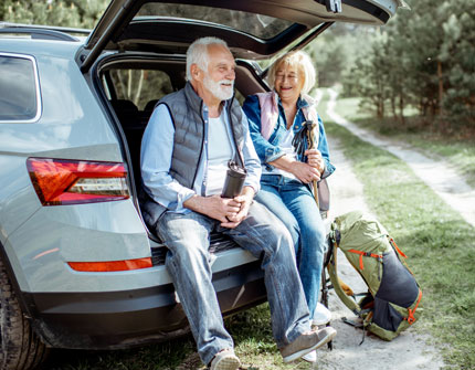 Senior couple sit in the trunk of their hatchback vehicle.