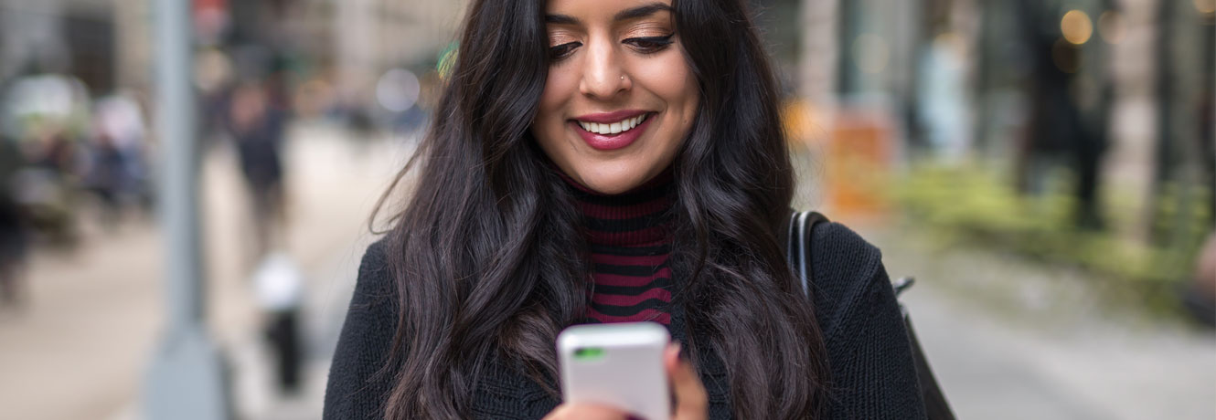 Woman smiles while looking at her phone in a downtown area.