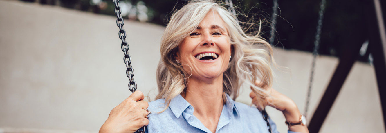 Older woman smiles while she plays on a swing set.
