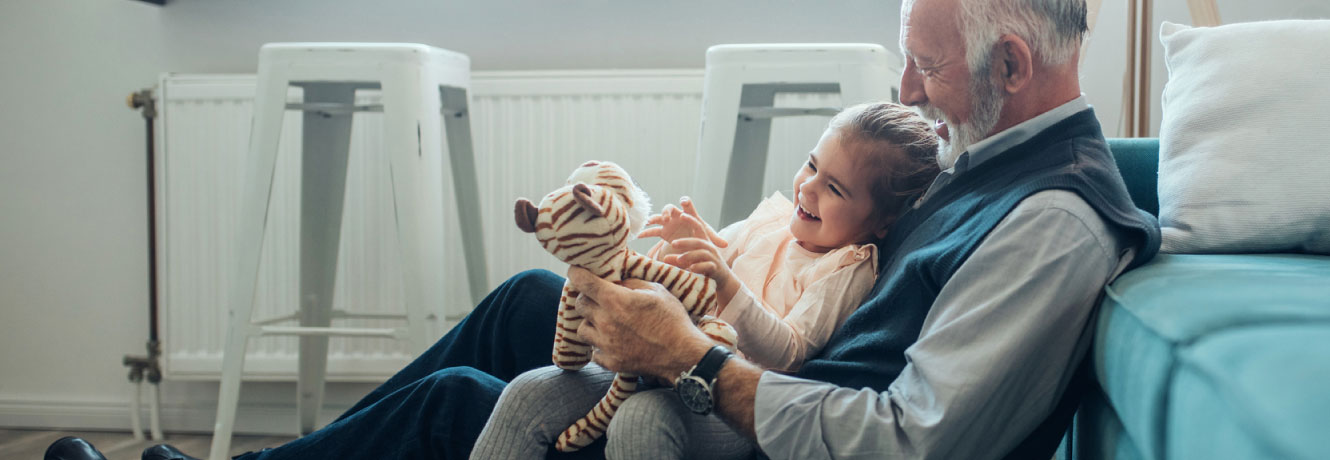 A grandfather and granddaughter laugh as they enjoy the imaginative play with a stuffed tiger.